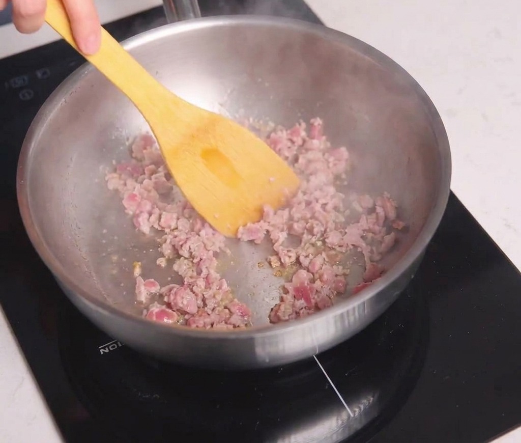 フライパンで黄色いヘラを使い、挽肉を細かくほぐしながら焼き色がつくまで炒めている様子