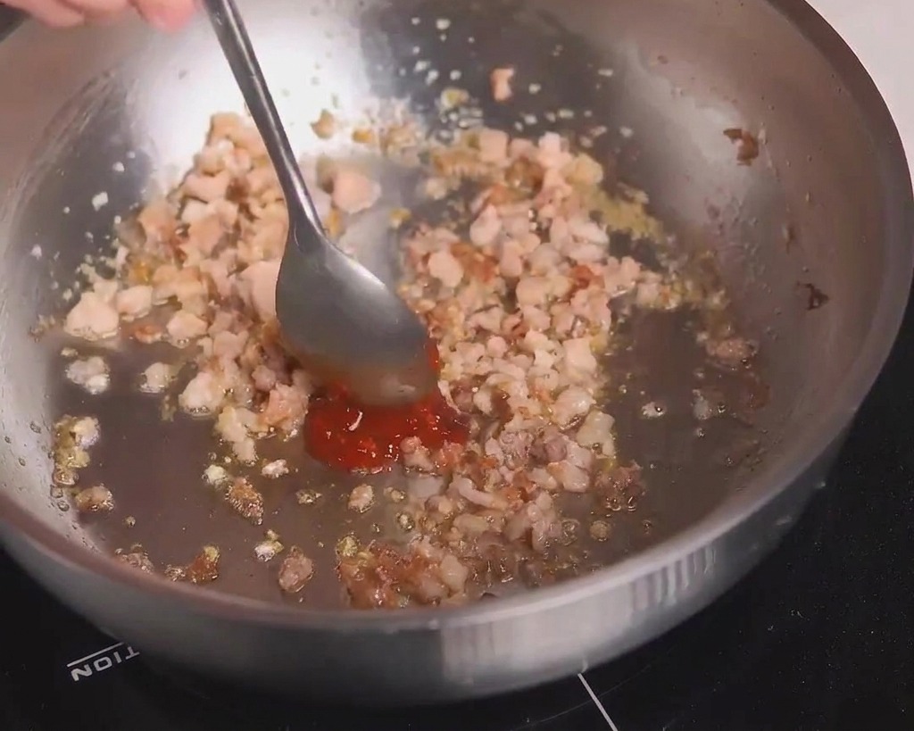 炒めた挽肉にスプーンで赤い豆板醤を加えて混ぜ合わせている様子