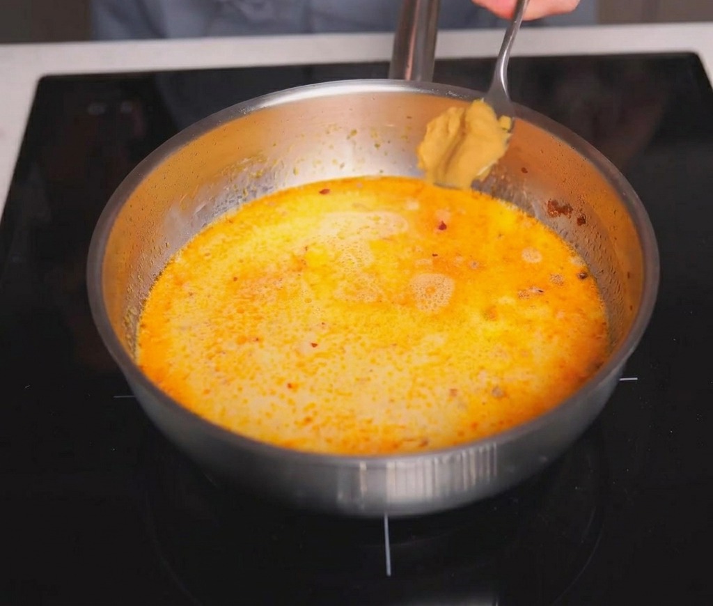 煮え立つクリーミーなスープにスプーン一杯の味噌を加えている様子