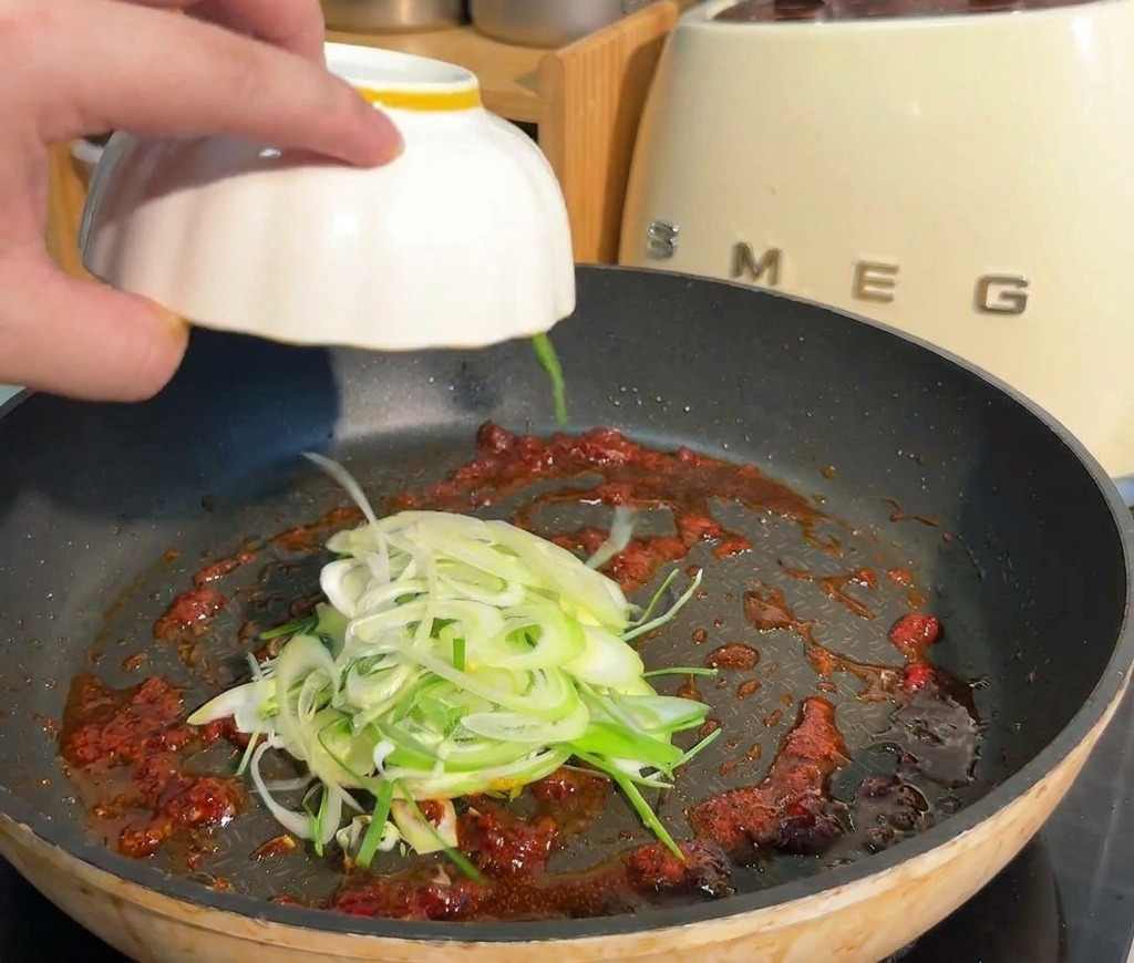 炒めた豆板醤の中に、刻んだ長ねぎを投入している様子。