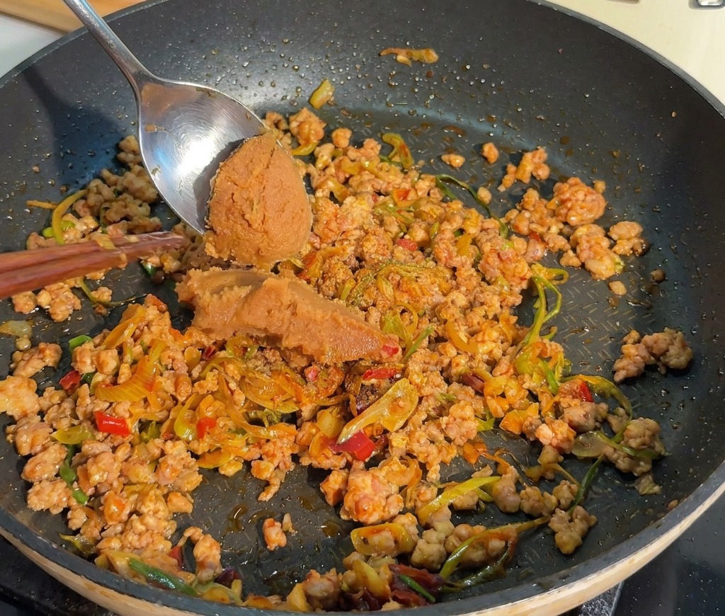 炒めた肉の上に赤味噌と粉唐辛子を加え、混ぜ合わせる様子。