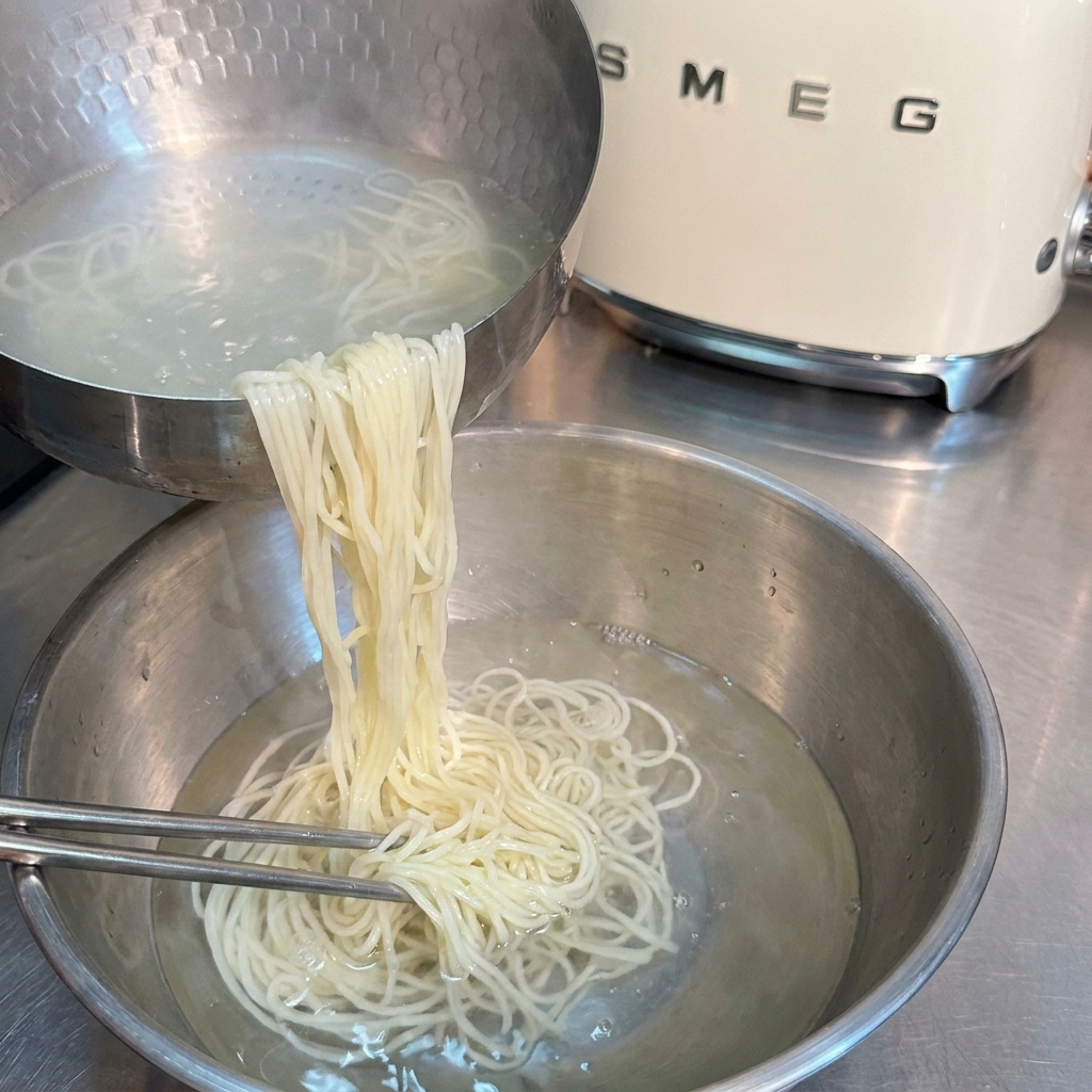 茹で上がった麺をザルに上げ、冷水で揉み洗いしている様子。