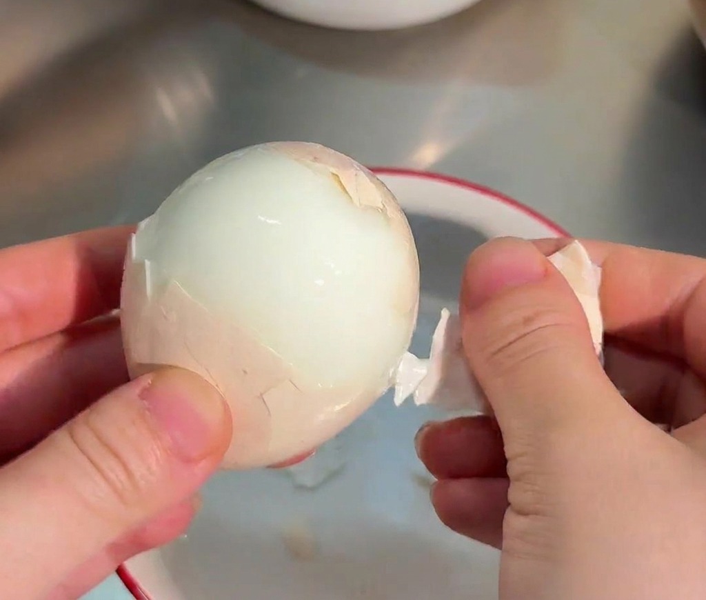 ツルンとした綺麗なゆで卵の殻を、手で丁寧にむいている様子。