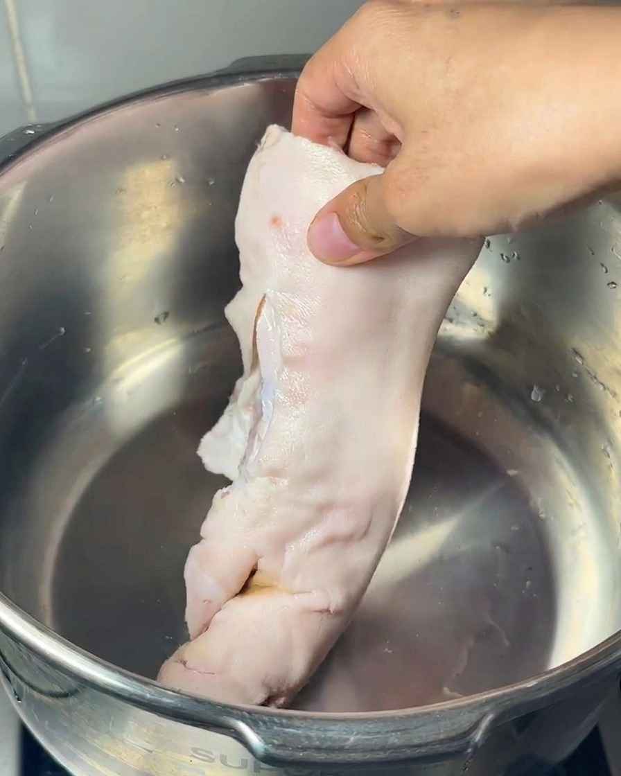 ステンレス鍋に生の豚足、大きな豚のげんこつ、鶏足を入れる様子。