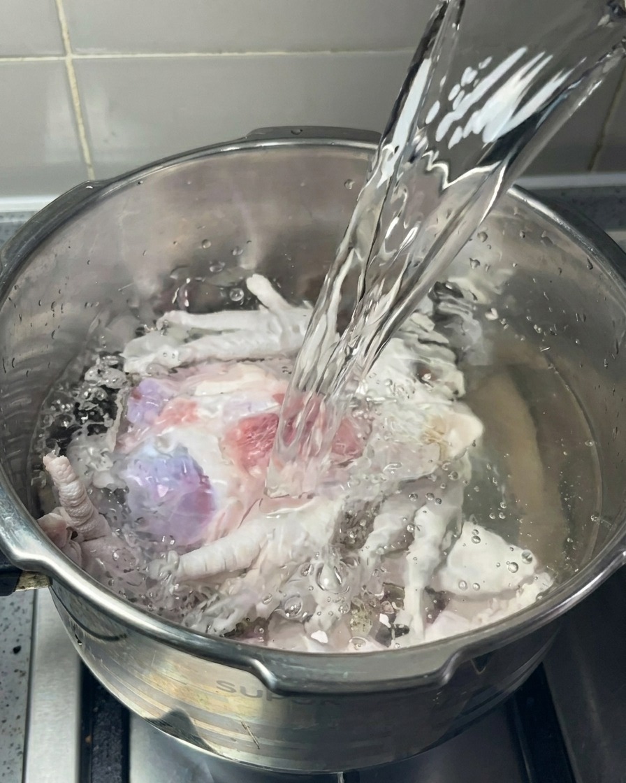 鍋に入った豚骨と鶏足に、蛇口から透明な水を注いでいる様子。