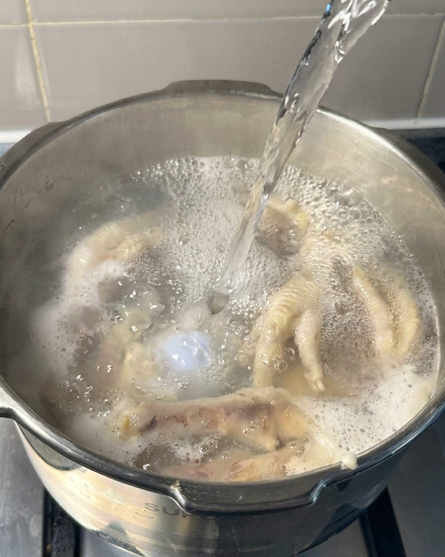 鶏足と豚骨が入った鍋に、沸騰したお湯を注ぎ足している様子。