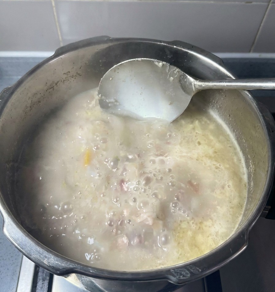 お玉で乳白色のスープを混ぜている様子。肉や脂の粒が混ざり合っている。