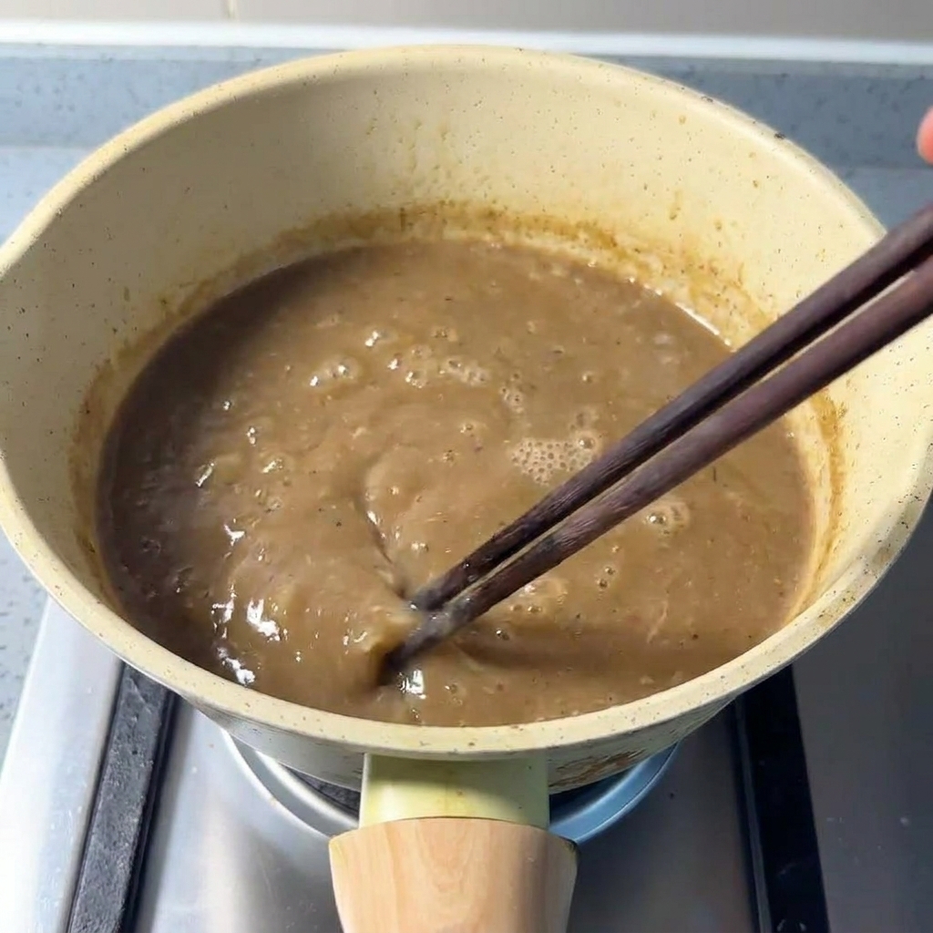 箸でスープと魚粉を混ぜながらじっくり加熱している様子