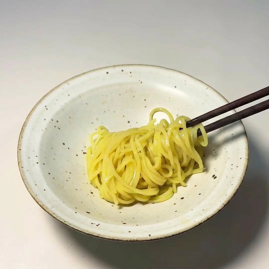 箸で茹で上がった太麺を器に丁寧に盛り付けている様子