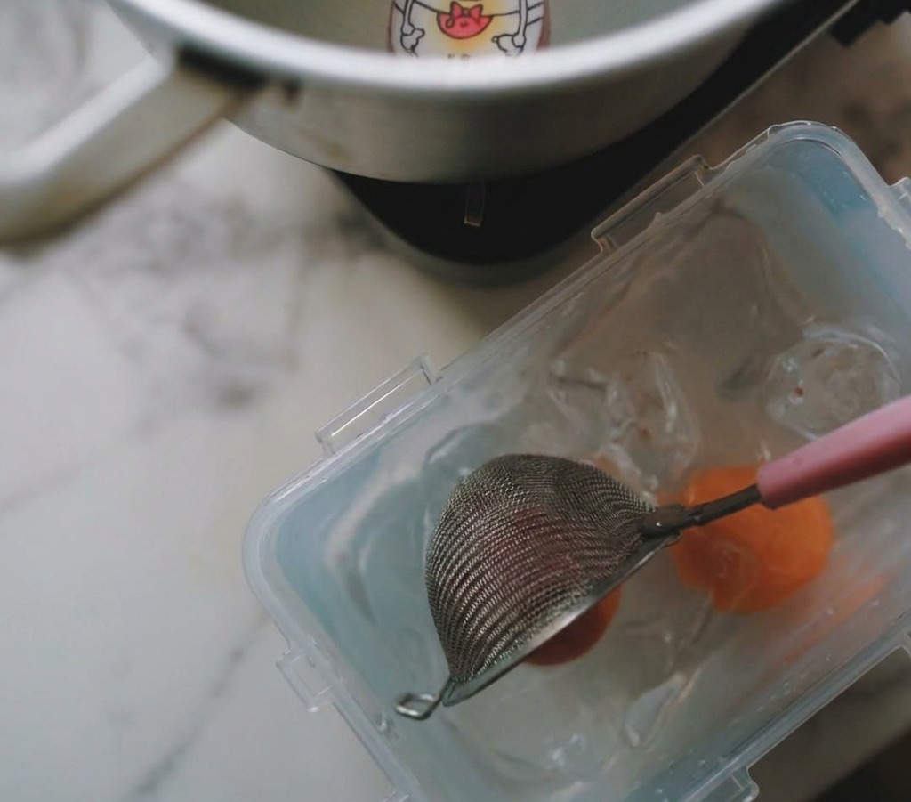 網じゃくしで鍋から卵をすくい上げ、氷水の入った容器に移している様子。