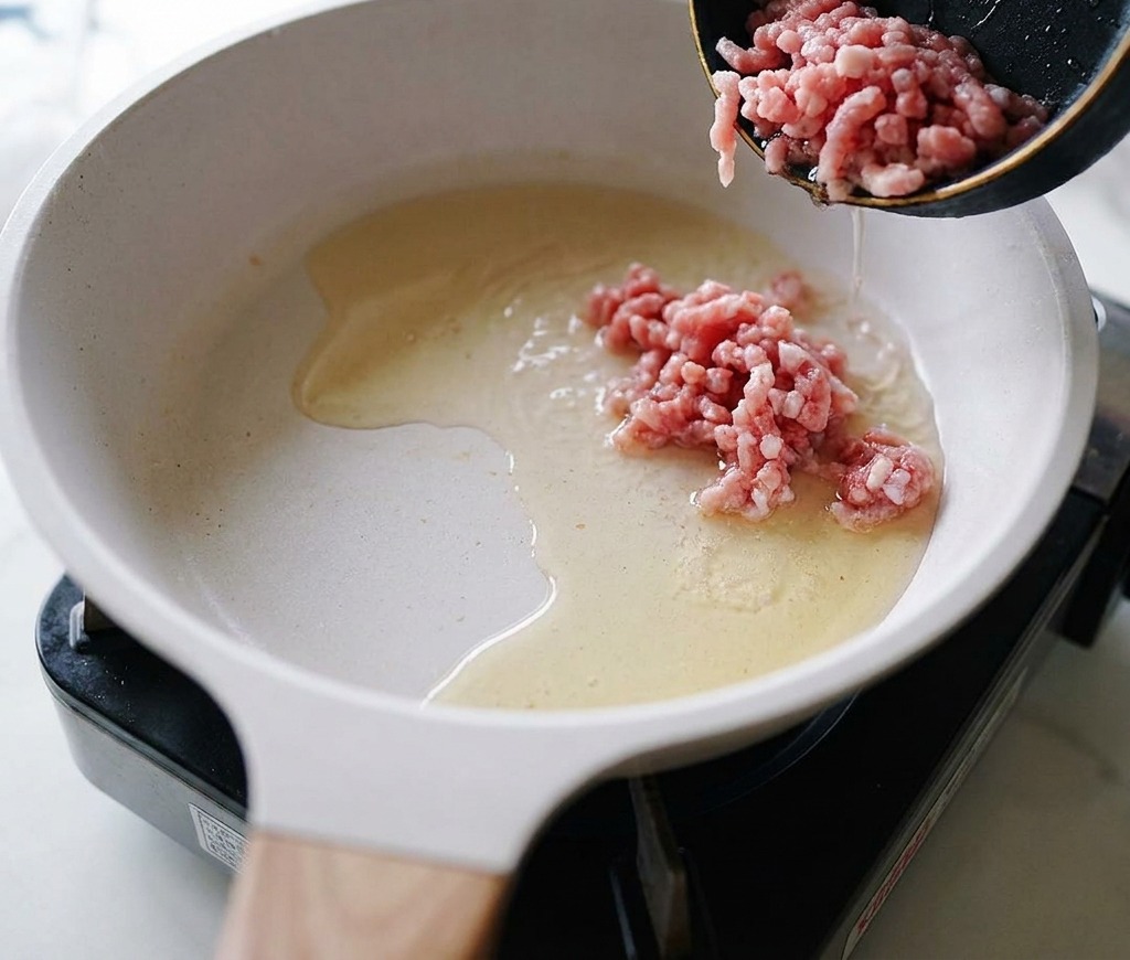 熱したフライパンに生の豚ひき肉を入れ、炒め始めようとしている場面。