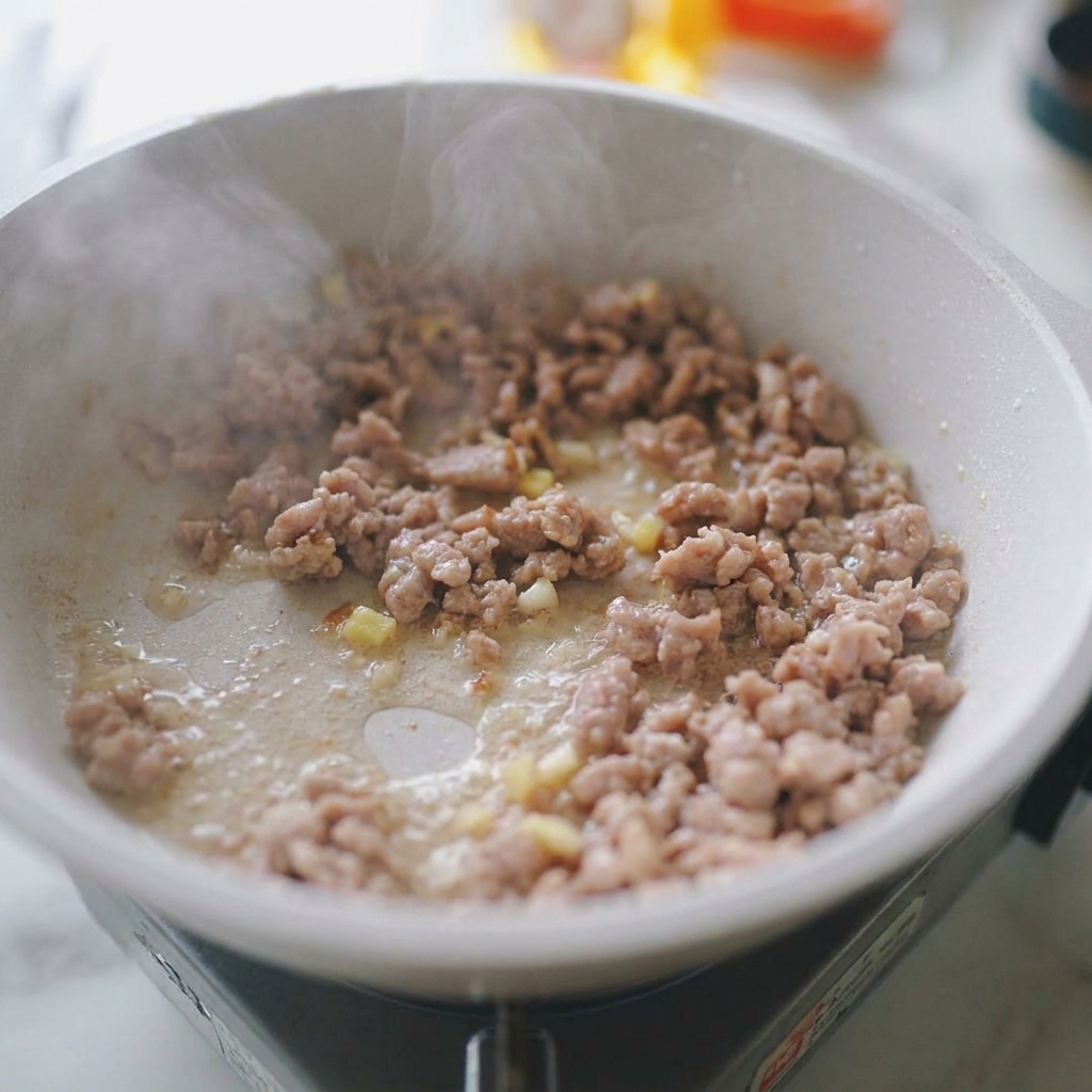 色づいた挽肉に、みじん切りのにんにくと生姜が加わり、香ばしく炒められている様子。