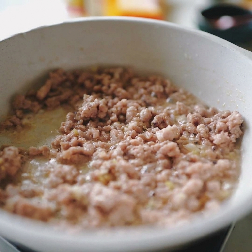挽肉と薄切りにした玉ねぎをフライパンで一緒に炒め合わせている様子。