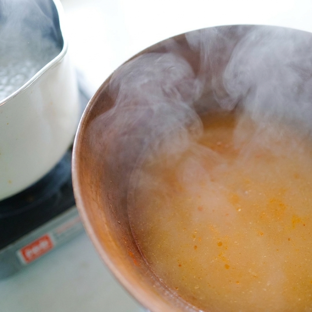 味噌だれが入った器に、お玉で熱々の茹で汁を注ぎ入れている様子。