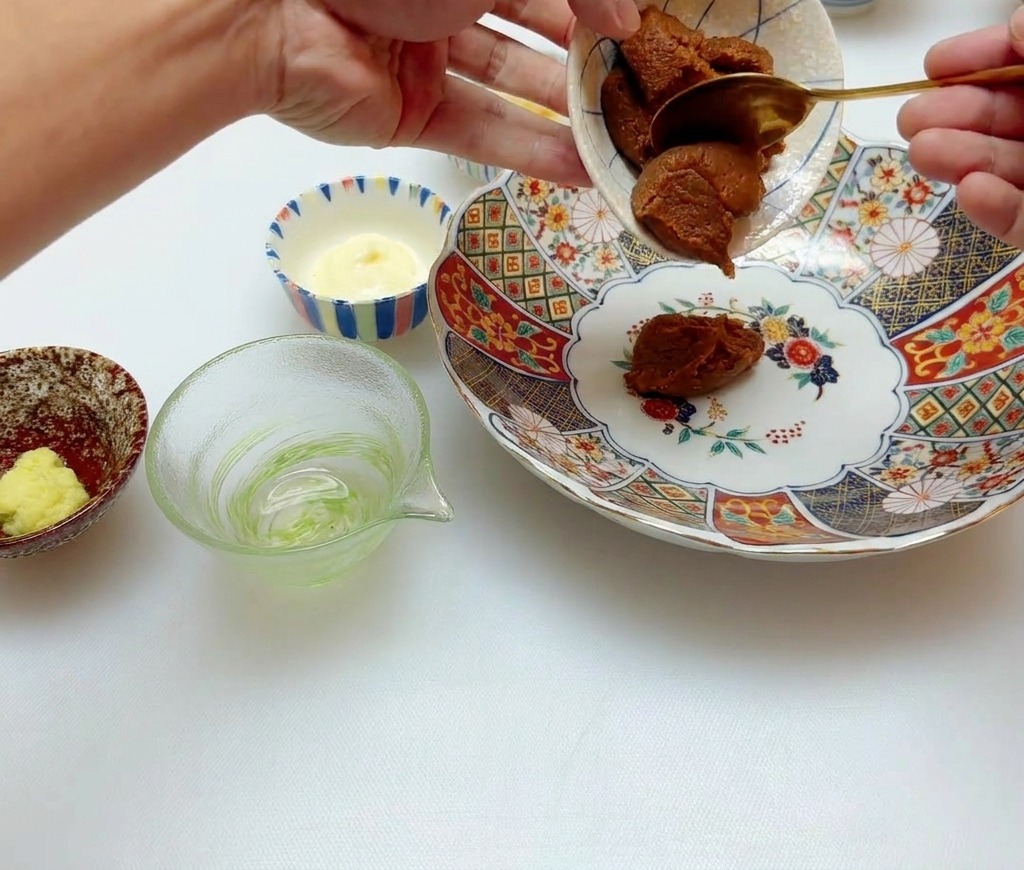 金色のスプーンで、赤味噌を小皿から花柄のボウルに移している様子。