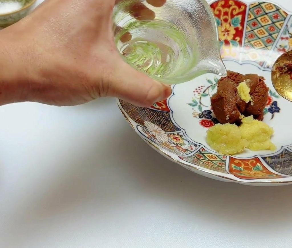 小さなガラス容器から、味噌と生姜が入ったボウルにサラダ油を注いでいる様子。