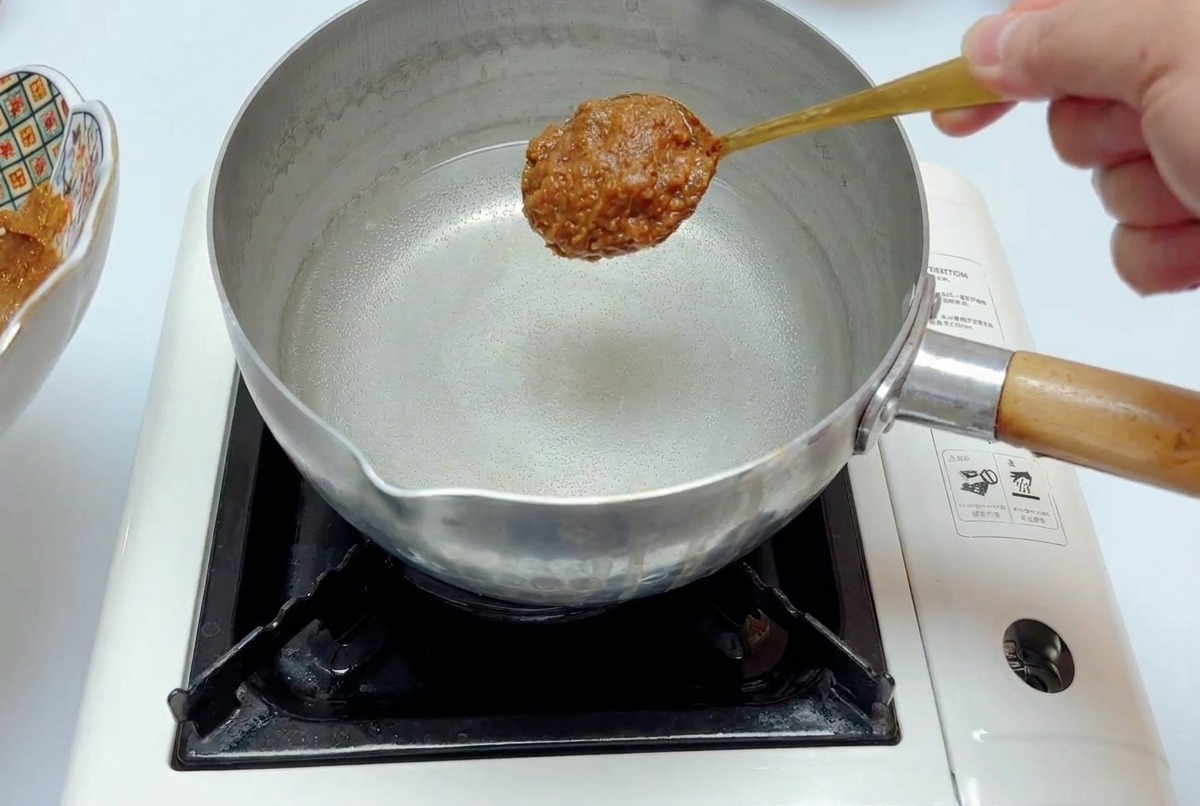 コンロにかけた鍋のお湯に、スプーン一杯の味噌だれを入れようとしている様子。