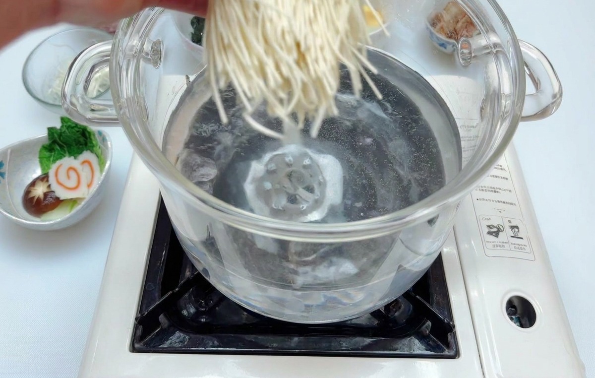 沸騰した鍋の中に、生の中華麺を一玉入れている様子。
