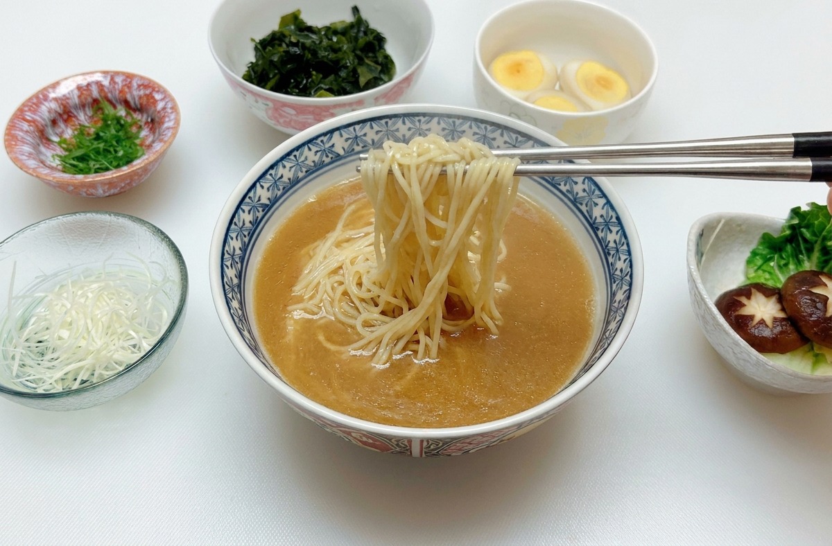 箸でどんぶりの中の麺を持ち上げ、中央に整えている様子。
