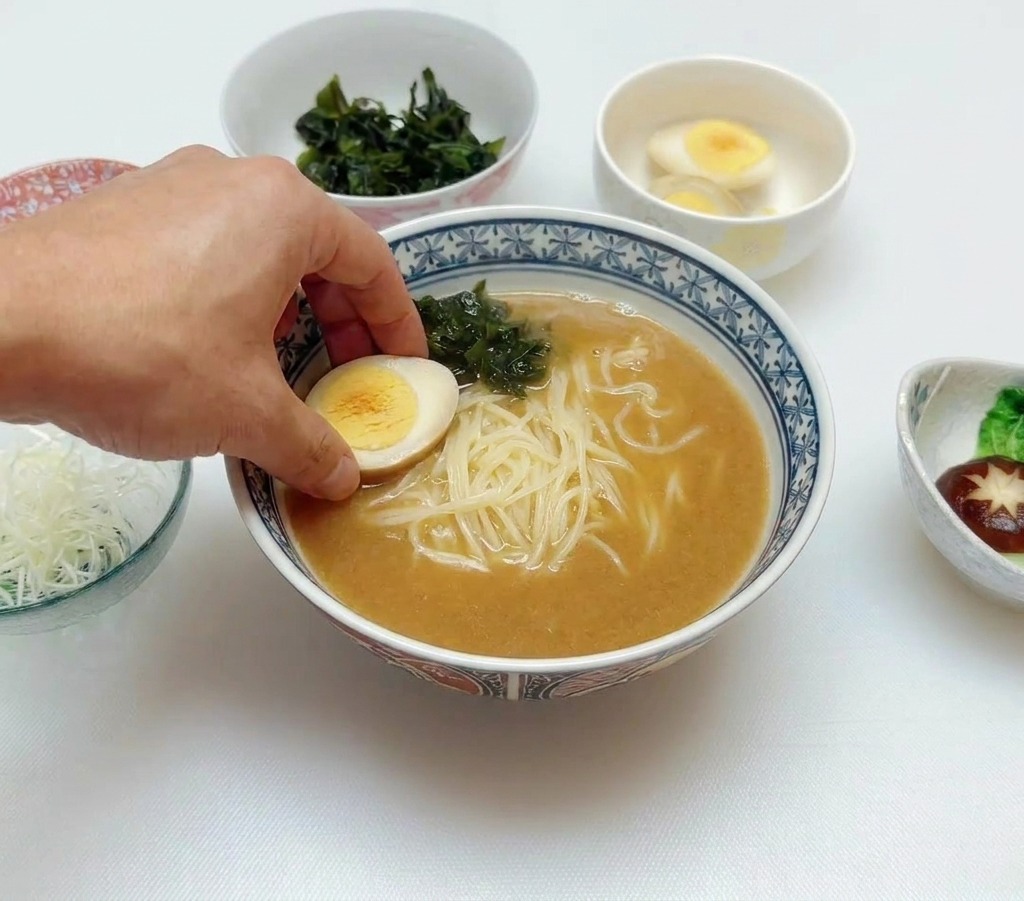麺とわかめがのった器に、半分に切った半熟卵を添えている様子。