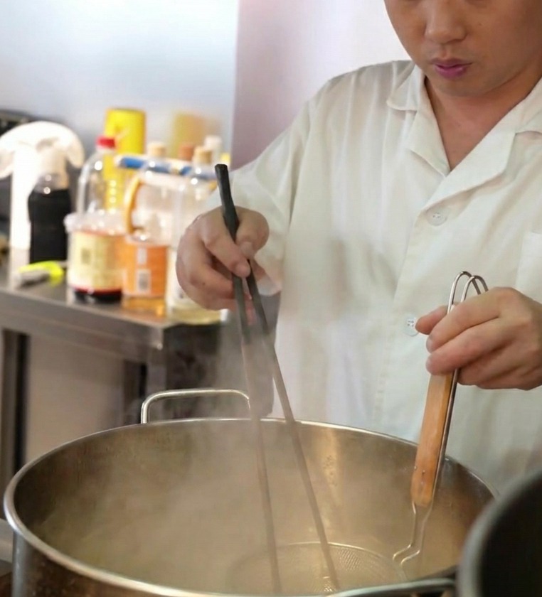 大きな鍋の熱湯にテボ(振りザル)に入れた麺を入れる様子