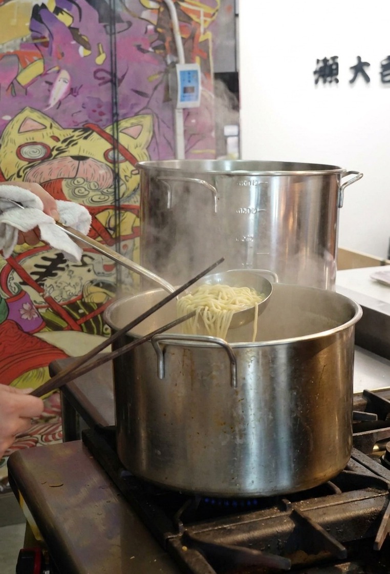 茹で上がった麺をテボで持ち上げ、お湯を切る様子
