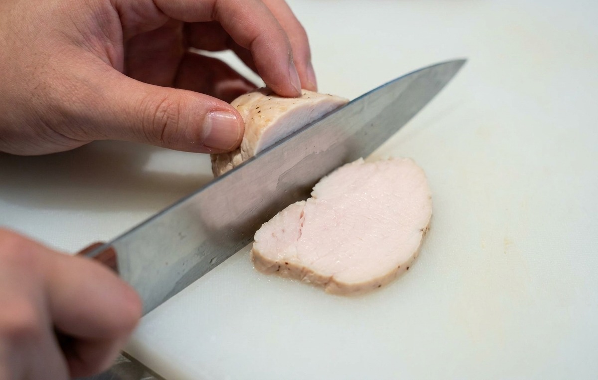 まな板の上で低温調理された鶏むね肉を薄くスライスする様子