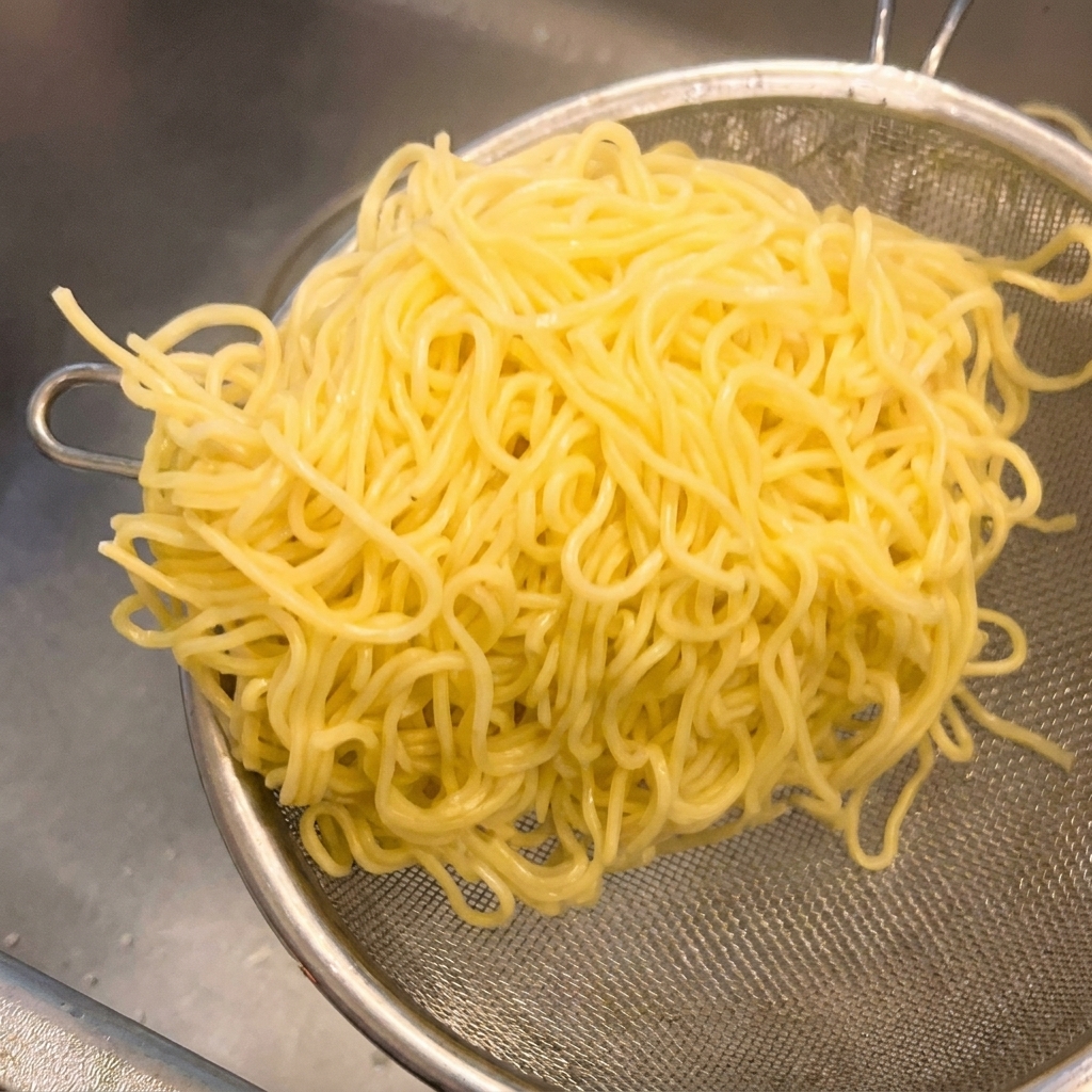 茹で上がった中華麺をざるに入れ、しっかり振って水気を切っている様子。