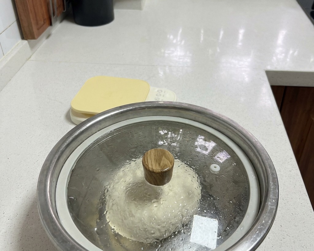 木製の取っ手がついたガラスの蓋を被せた、水滴のついたボウルの中の生地。