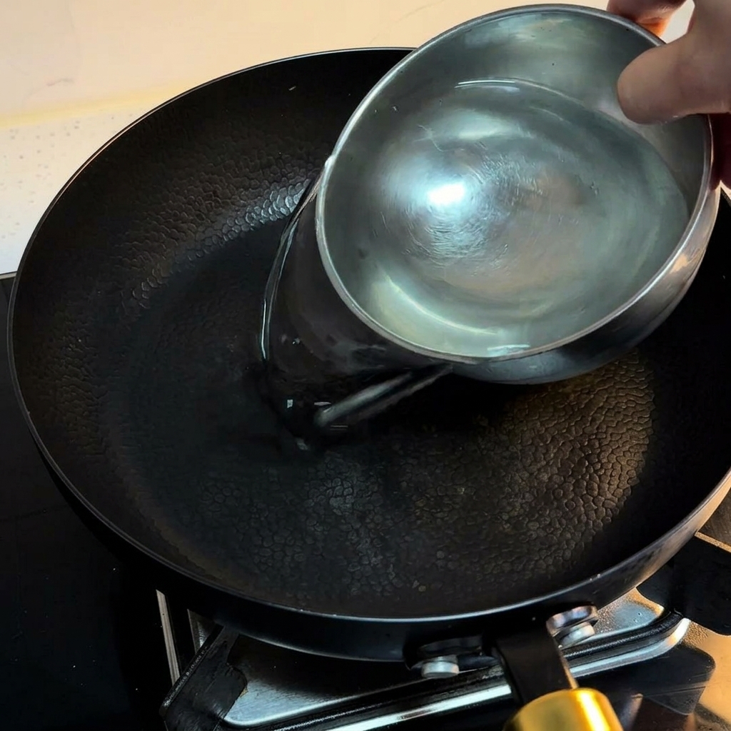 黒いフライパンに水を注ぎ、火にかける様子。