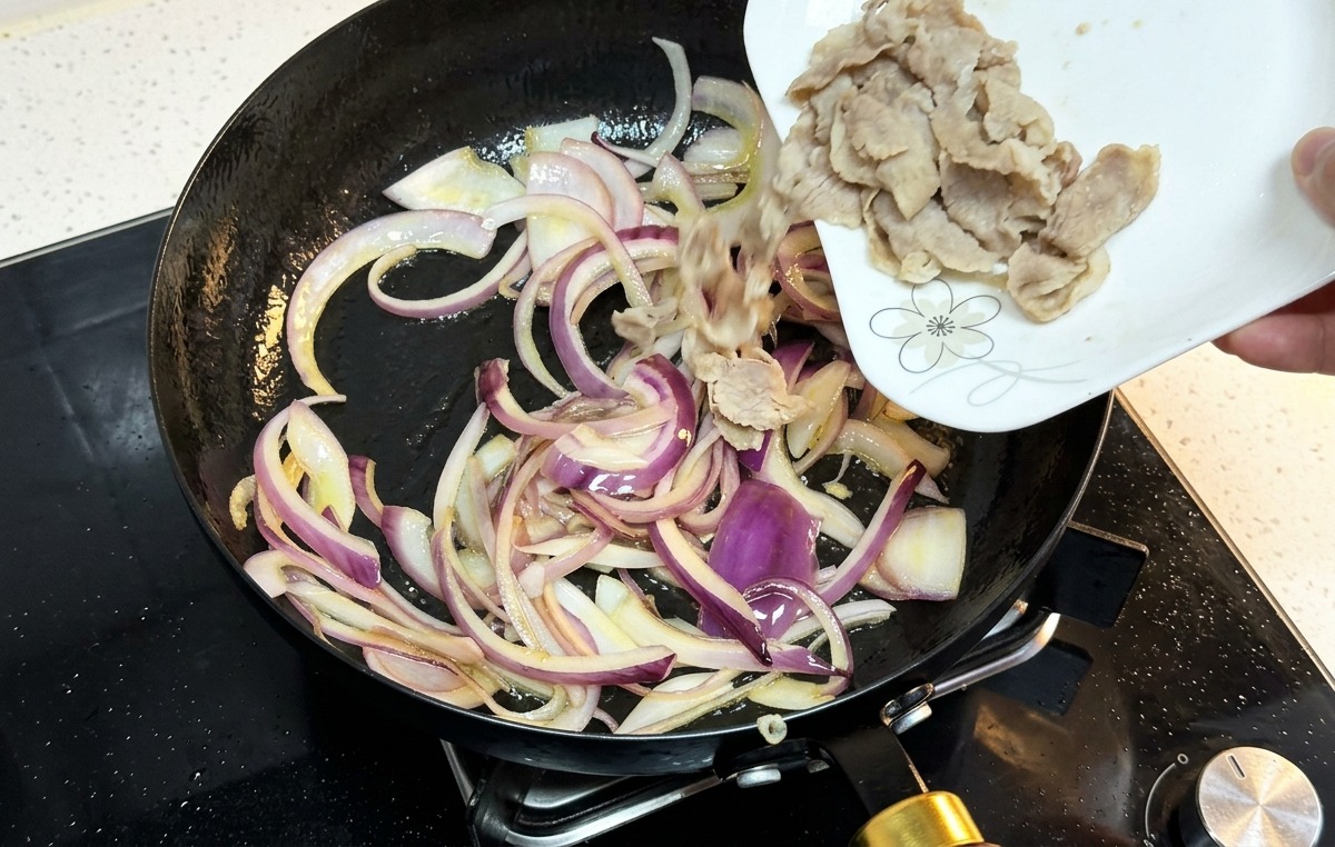 炒めた玉ねぎの入ったフライパンに、茹でた牛肉を加える様子。