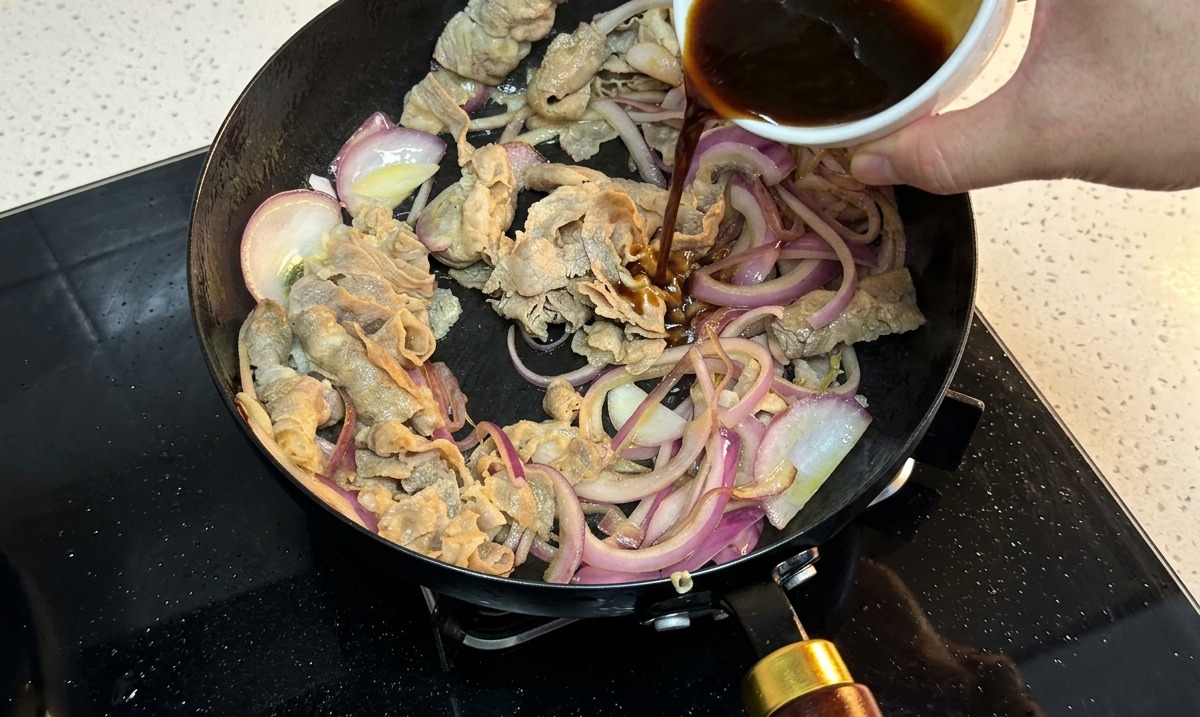牛肉と玉ねぎが入ったフライパンに、合わせたタレを注いでいる様子。