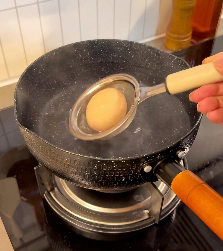 おたまを使って卵をそっとお湯に入れている様子。
