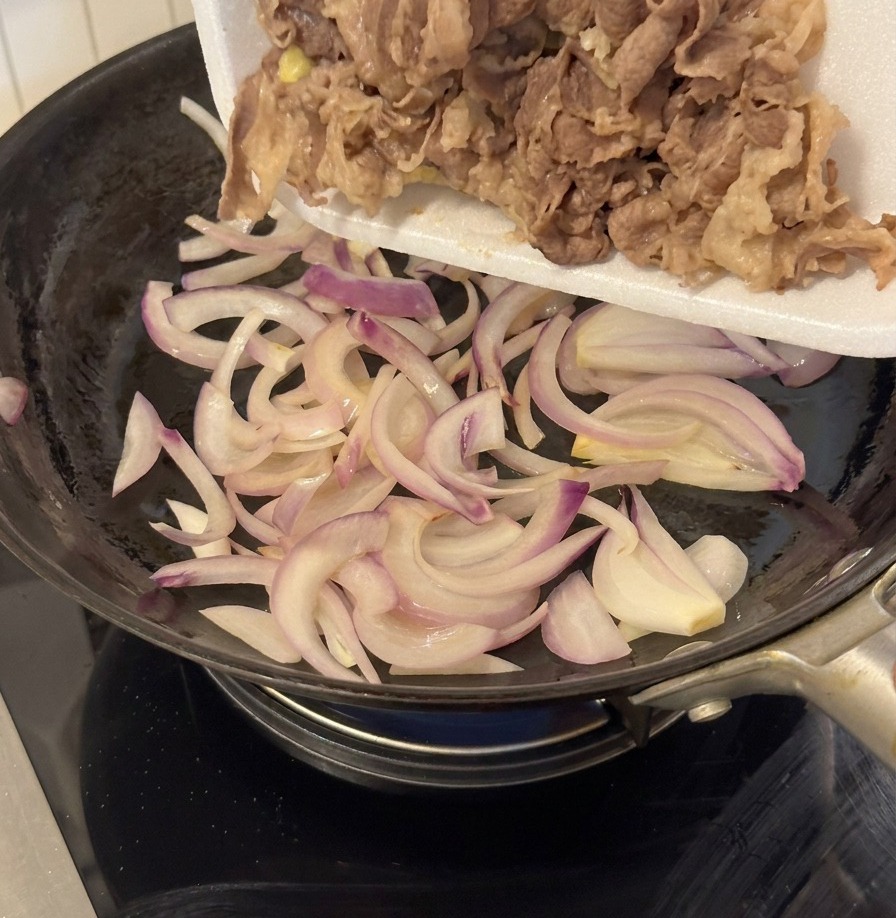 炒めた玉ねぎの入ったフライパンに牛肉とタレを入れる様子。