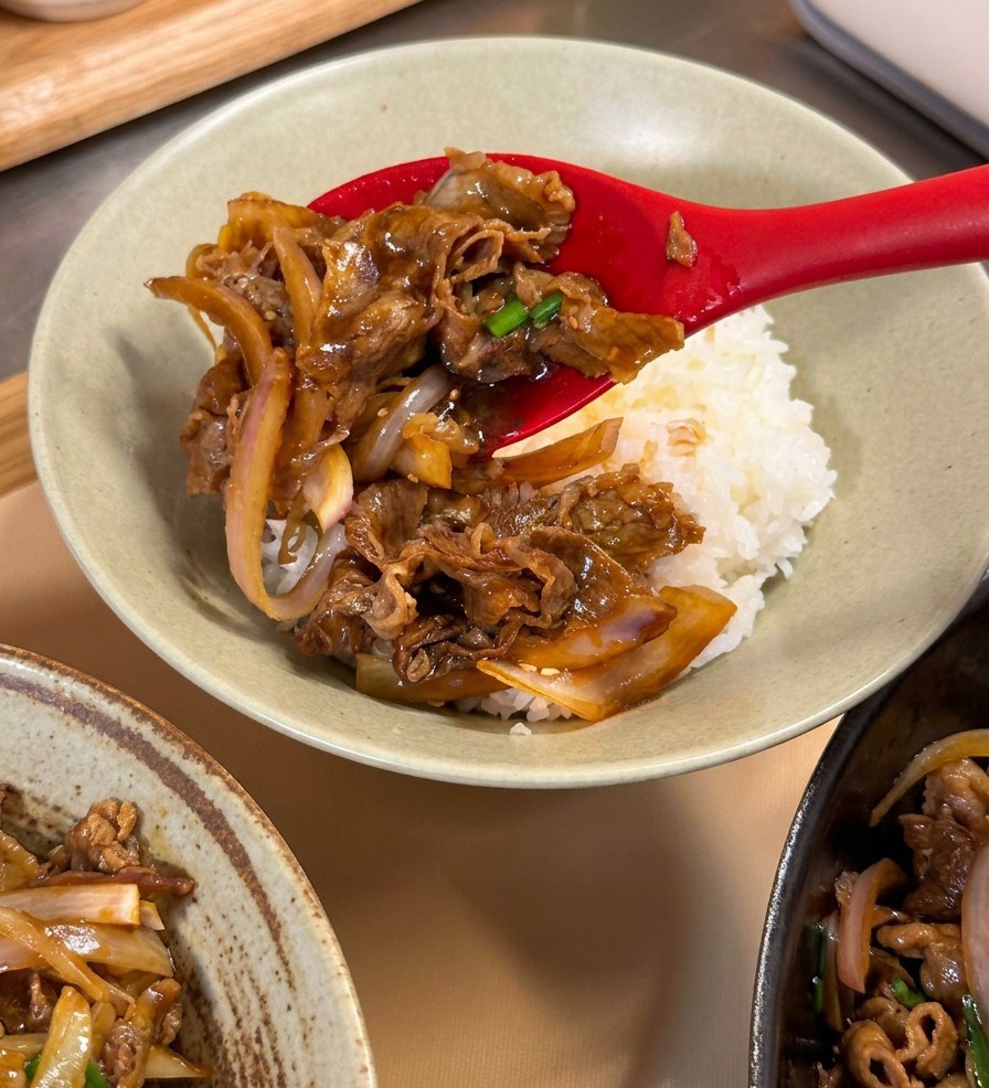 白いご飯の上に牛肉を盛り付けている様子。