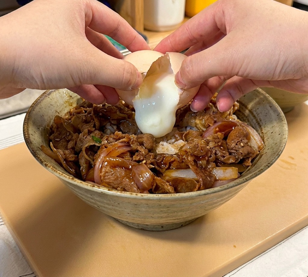 牛丼の真ん中に温泉卵を割り落としている様子。