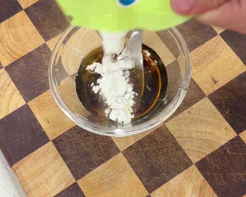 調味料の入ったボウルに白い片栗粉を加え、スプーンで混ぜる様子。