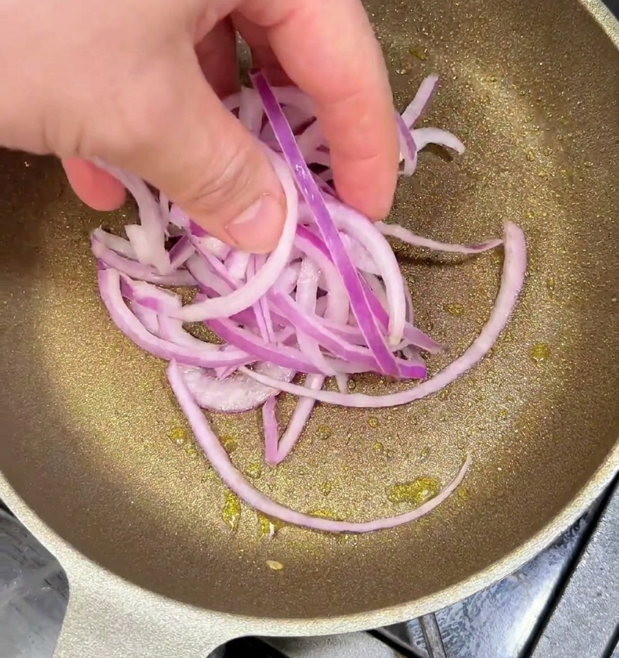 フライパンでスライスした赤玉ねぎを炒め、少し焦げ目がつき始めている様子。