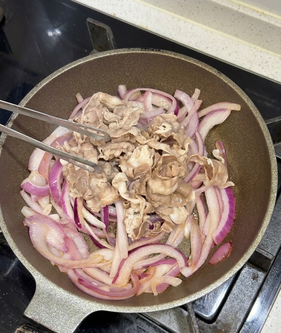 炒めた赤玉ねぎが入ったフライパンに、湯通しした牛肉を加える様子。