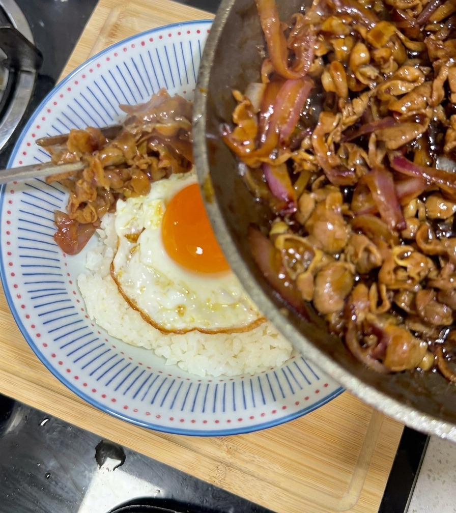 ご飯と目玉焼きの上に、たっぷりの照り焼きビーフを盛り付けている様子。