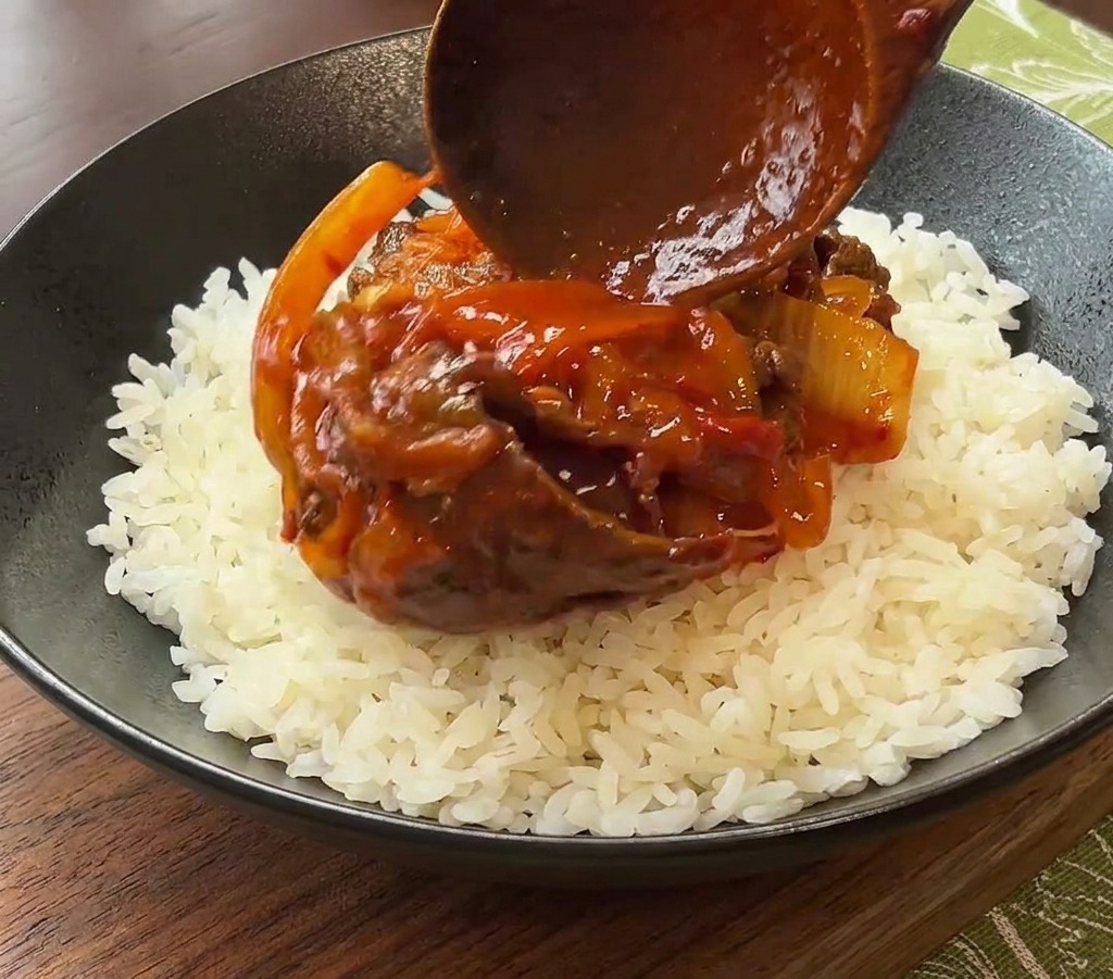 黒い器に盛られたご飯の上に、完成したキムチ牛肉を盛り付ける様子。