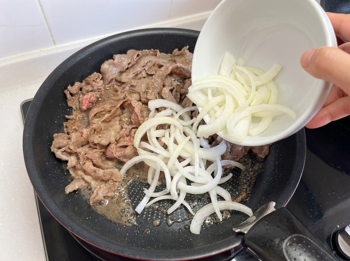 焼いた肉に玉ねぎとにんにくを加える様子