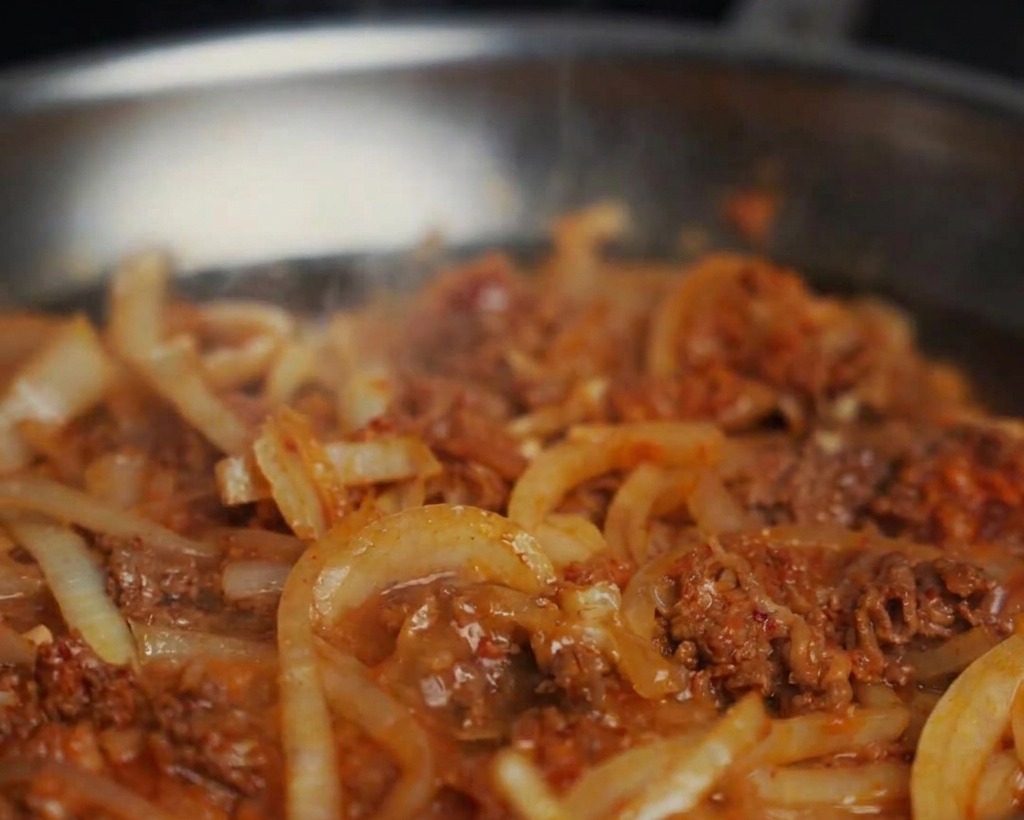 炒めた牛肉と玉ねぎが入ったフライパンに水が注がれ、グツグツと煮立つソースができている様子。