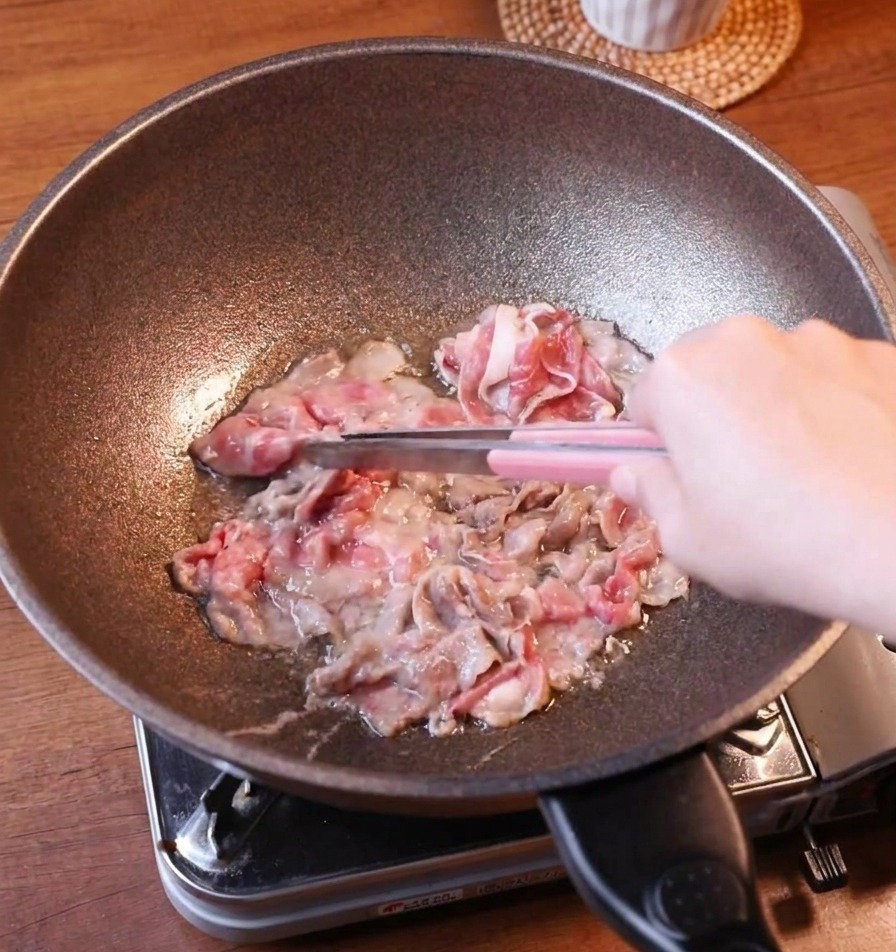 焼き色のついた牛肉をトングでフライパンから取り出している様子。
