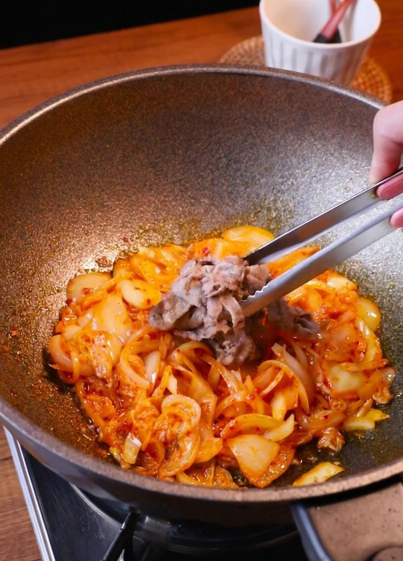 炒めたキムチと玉ねぎが入ったフライパンに牛肉を戻す様子。