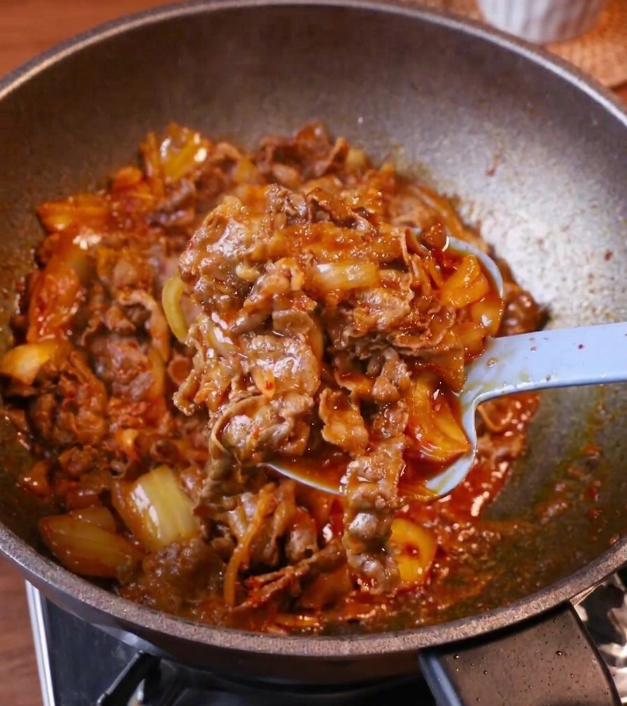 ご飯の上にたっぷりのキムチ牛肉を盛り付け、中央に卵黄をのせる様子。