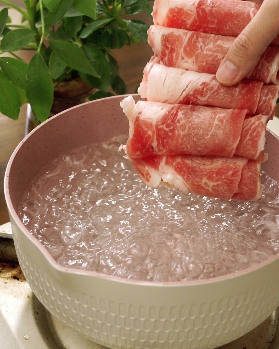 沸騰した鍋のお湯に、生の牛バラ薄切り肉を入れている様子。