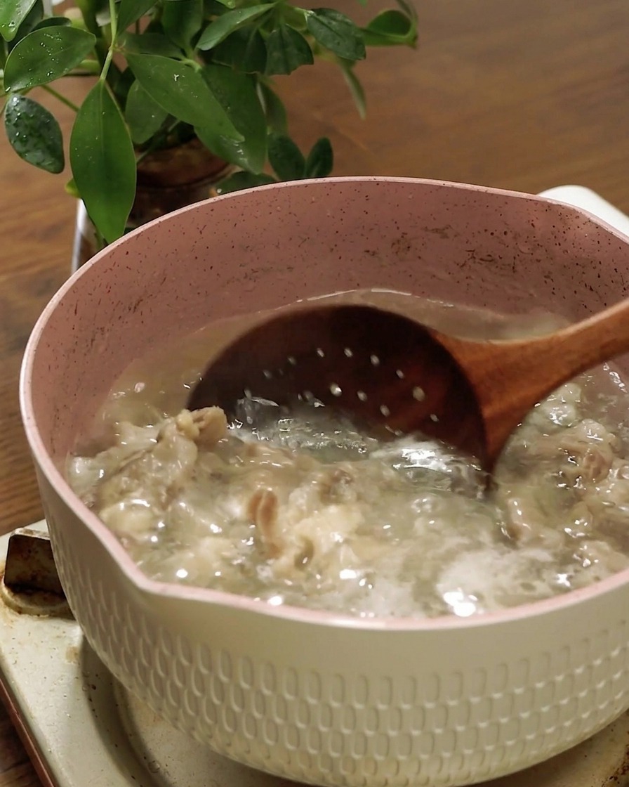 木製の穴あきお玉を使って、茹で上がった牛バラ肉を沸騰したお湯からすくい上げている様子。