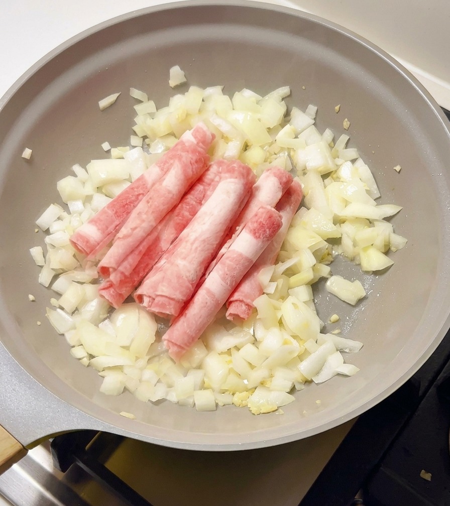 炒めた玉ねぎの入ったフライパンに、凍ったままの牛薄切り肉を加えている様子。