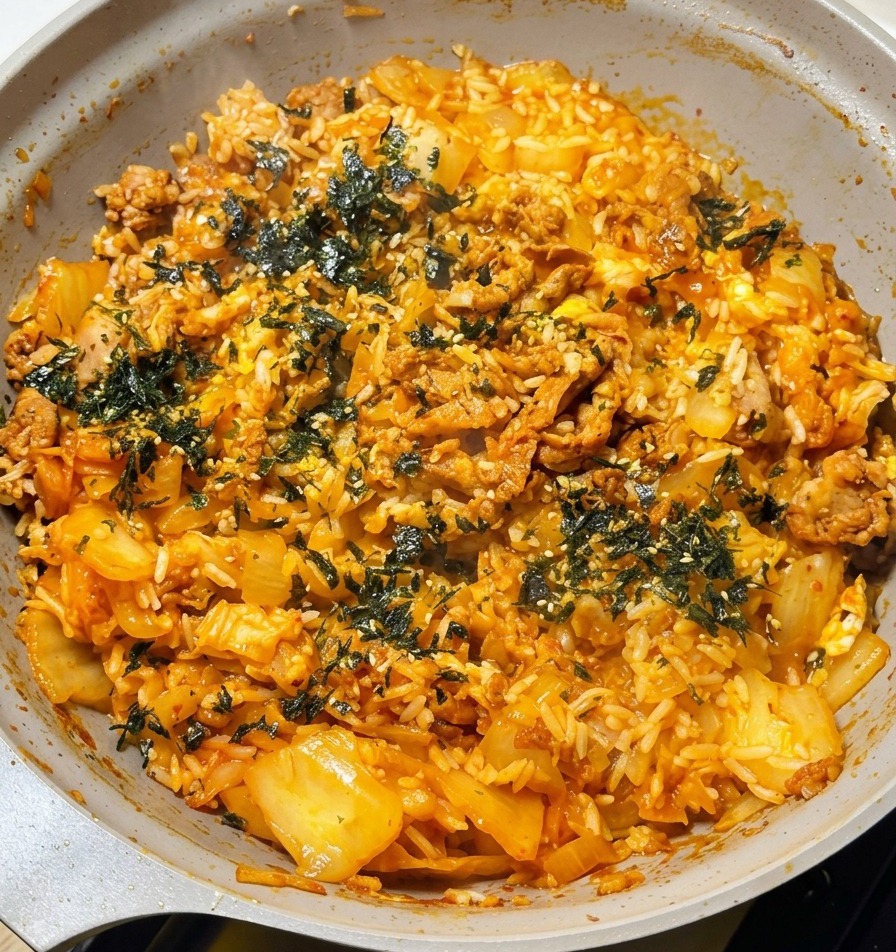 チーズがとろける熱々のキムチ牛肉チャーハンに、ちぎった韓国海苔をたっぷりと振りかけている手。